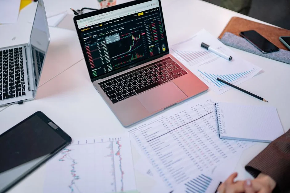 Person analyzes stock data with a smartphone and laptop, indoors.